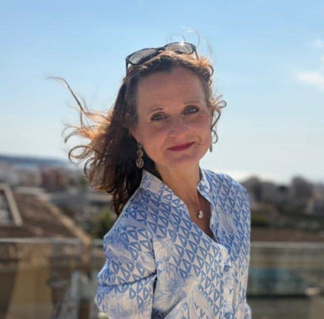 Frau im Freien mit Sonnenbrille, blauer Musterbluse, bei sonnigem Wetter.